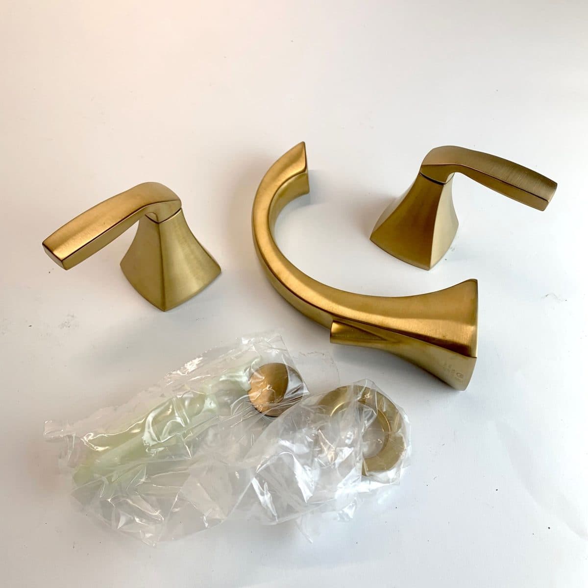 A brushed gold bathroom faucet unpacked on a table: the spout, two lever handles and bagged drain parts