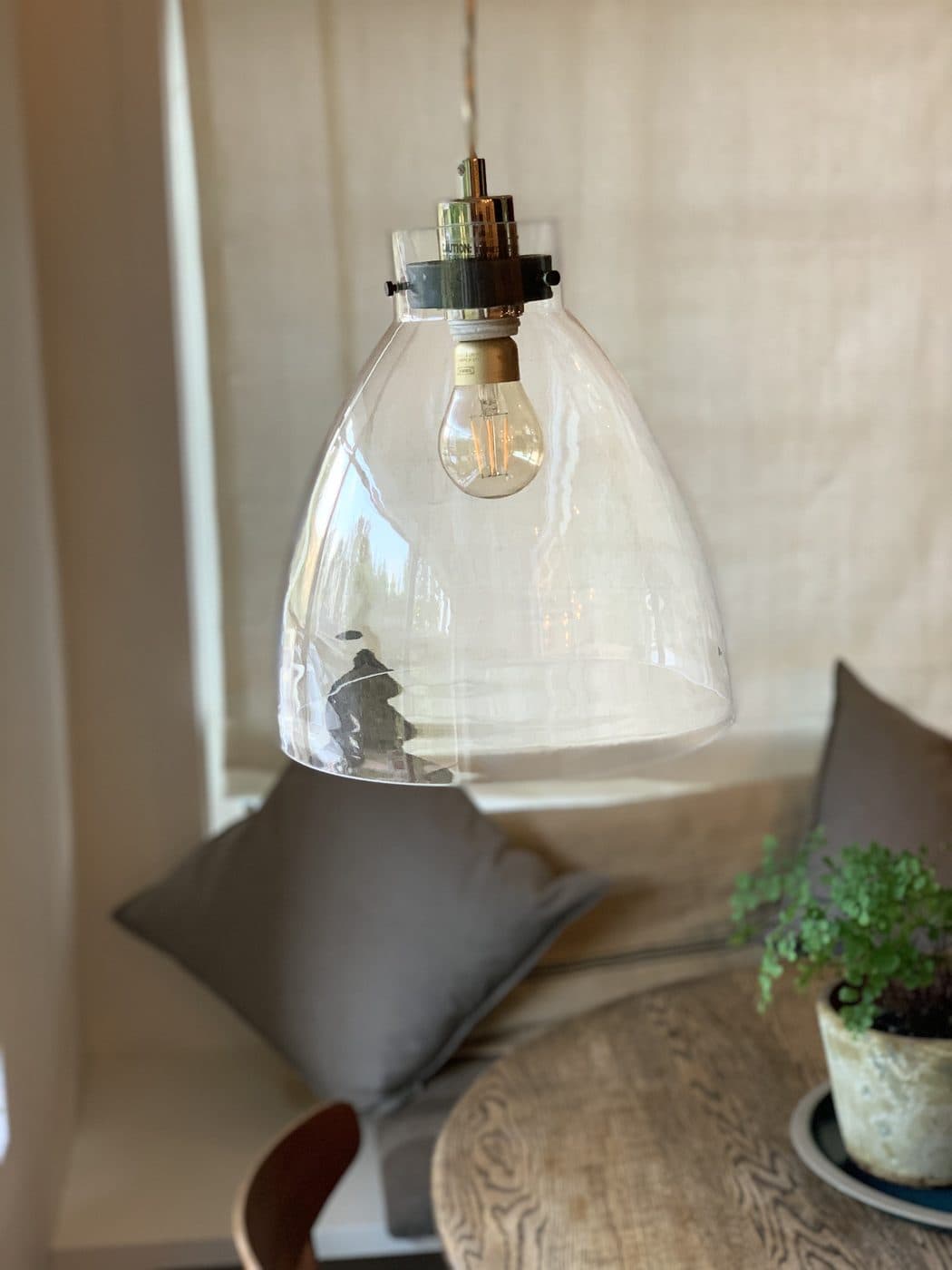 A clear glass pendant with an exposed filament bulb hanging over a breakfast table, the room behind it softly out of focus
