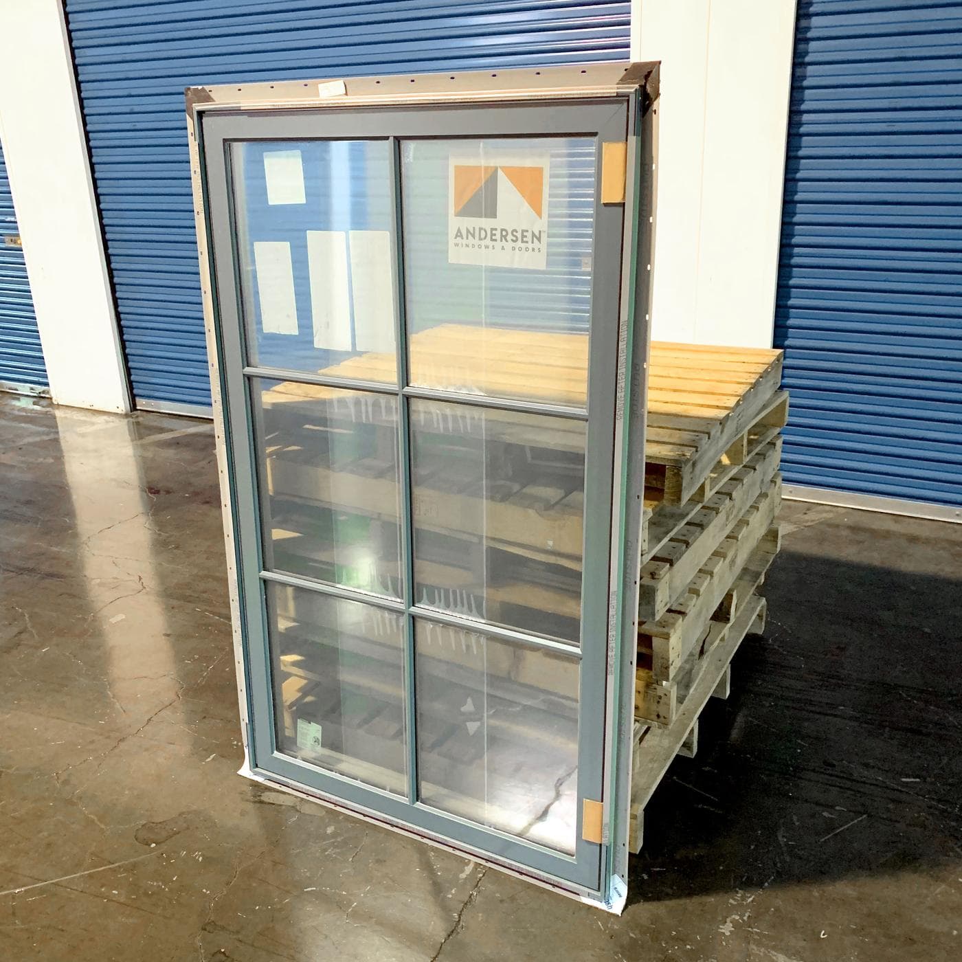 A new Andersen double-hung window standing on pallets in the warehouse, factory sticker and corner protection still in place