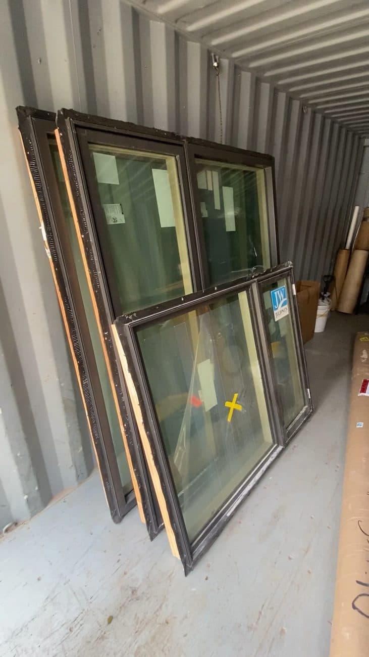 Dark-framed windows leaning upright against the wall of a storage container