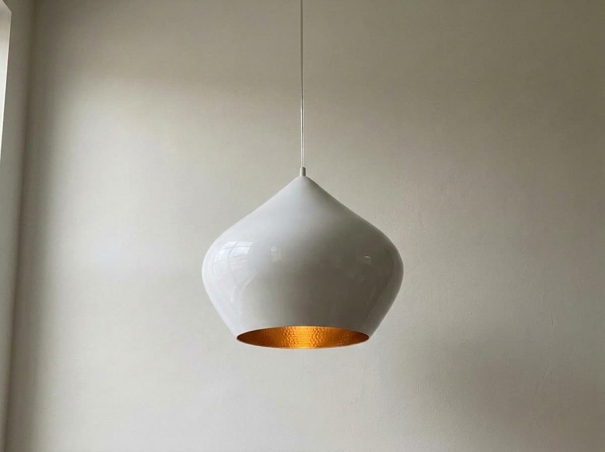 Tom Dixon Beat Stout pendant in white with the hand-beaten brass interior softly lit, hanging (AI-generated image)